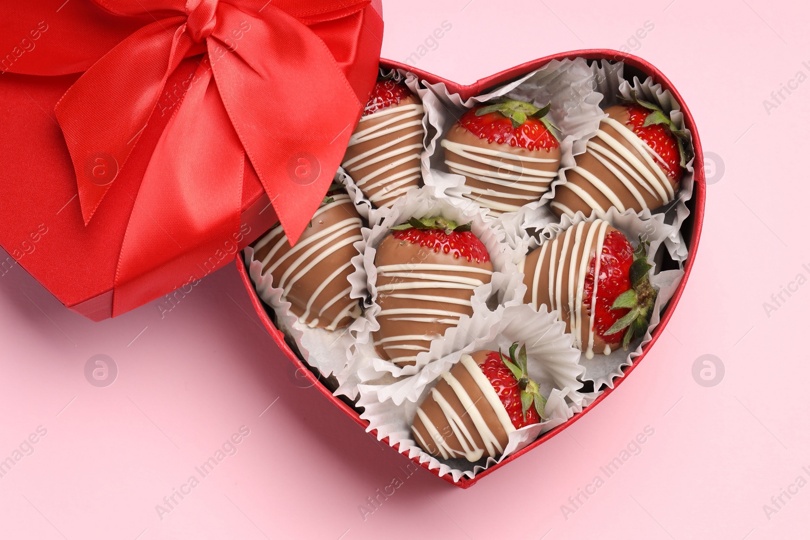 Photo of Heart shaped box with delicious chocolate covered strawberries on pink background, top view