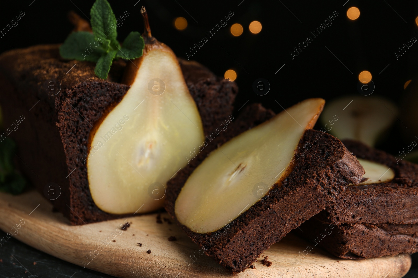 Photo of Tasty pear bread with mint on table against blurred lights, closeup. Homemade cake