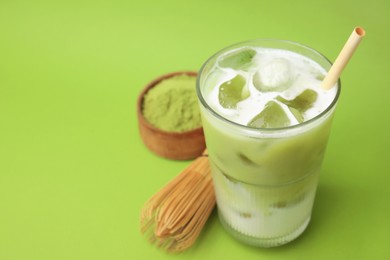 Glass of tasty iced matcha latte, bamboo whisk and powder on light green background, closeup. Space for text