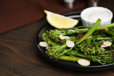 Photo of Tasty cooked broccolini with almonds, lemon and sauce on wooden table, closeup. Space for text