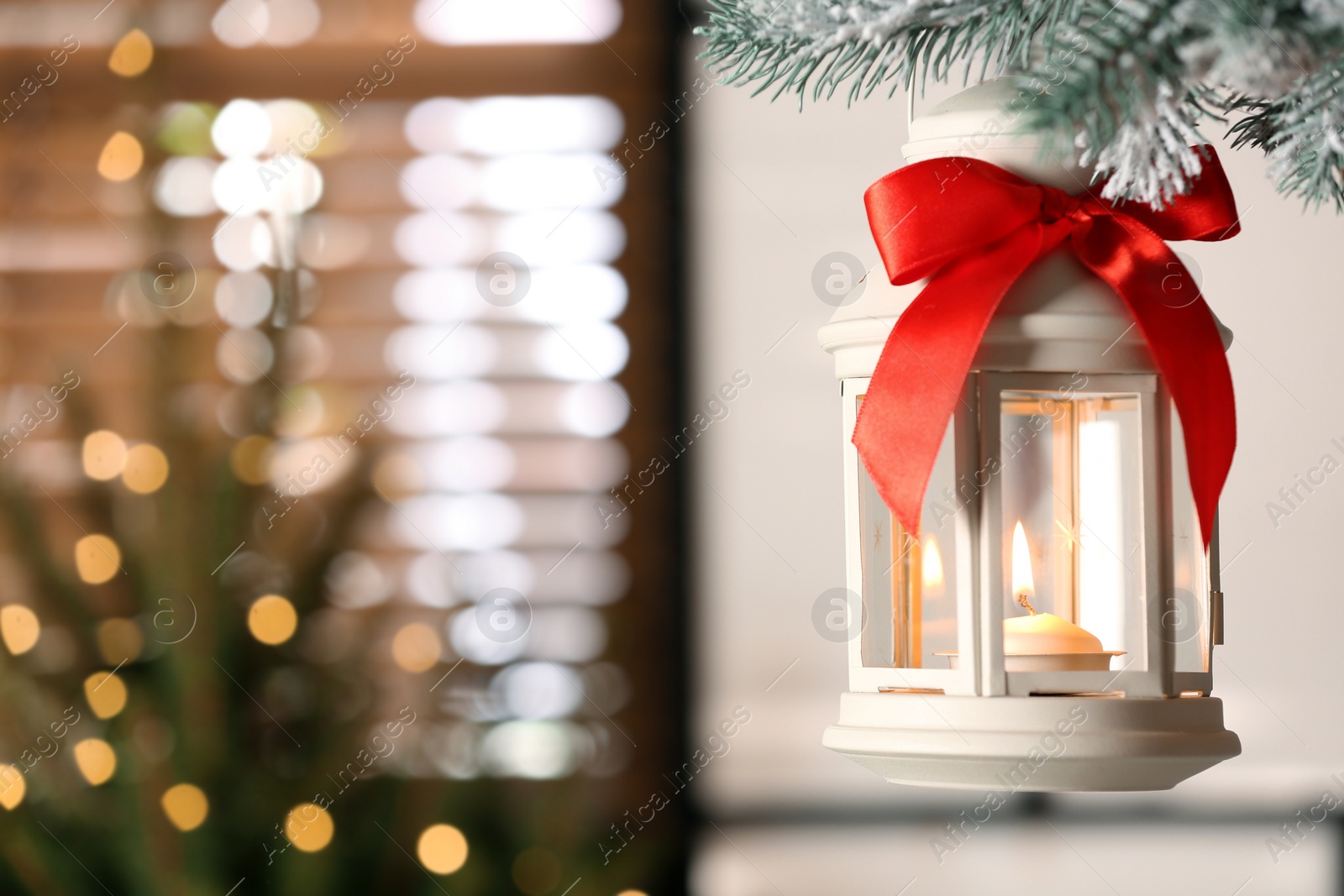 Photo of Beautiful Christmas lantern with burning candle hanging on fir tree branch in room. Space for text