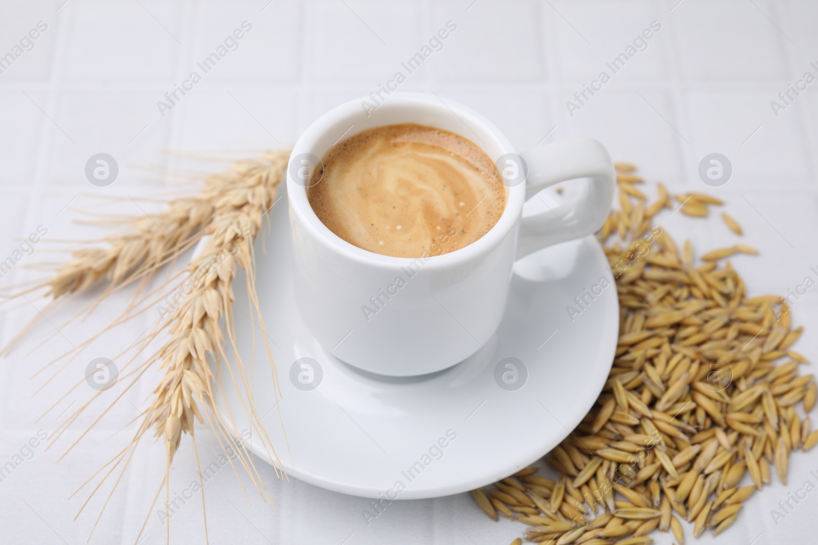 Photo of Cup of barley coffee, grains and spikes on white table, closeup