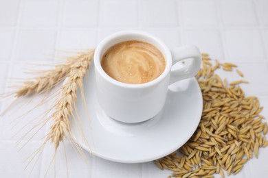 Cup of barley coffee, grains and spikes on white table, closeup