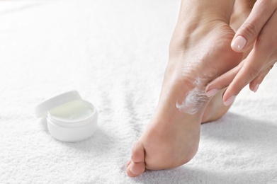 Woman applying foot cream on white towel, closeup with space for text. Spa treatment