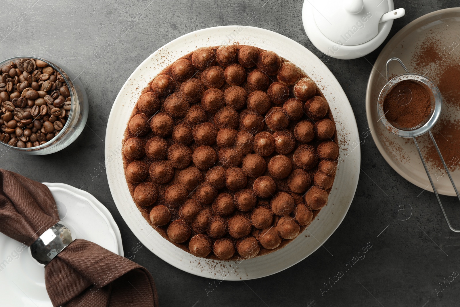 Photo of Delicious tiramisu cake with cocoa powder on grey table, flat lay