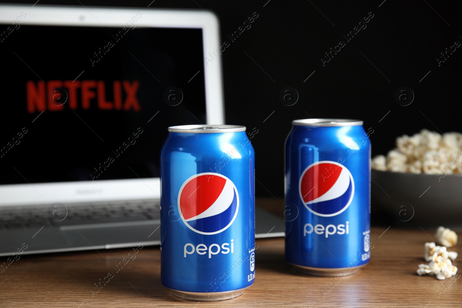 Photo of MYKOLAIV, UKRAINE - FEBRUARY 17, 2021: Cans of Pepsi and pop corn near laptop displaying Netflix on wooden table