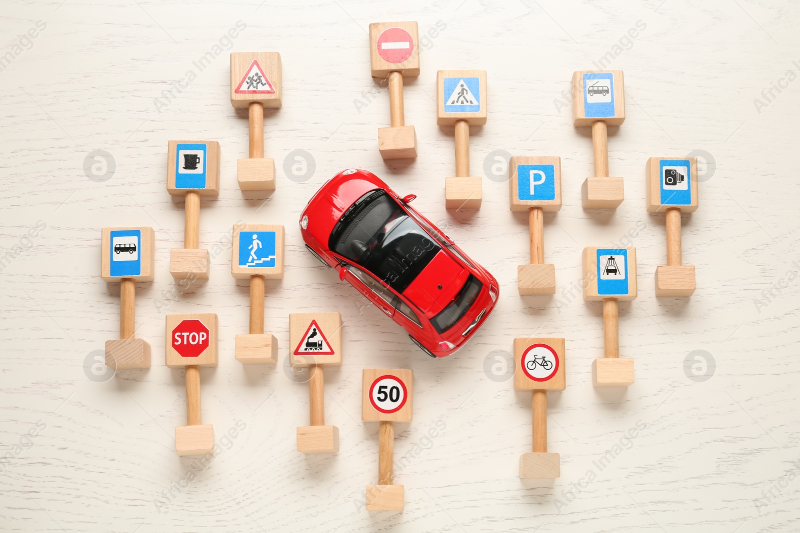 Photo of Many different miniature road signs and car on white wooden table, flat lay. Driving school