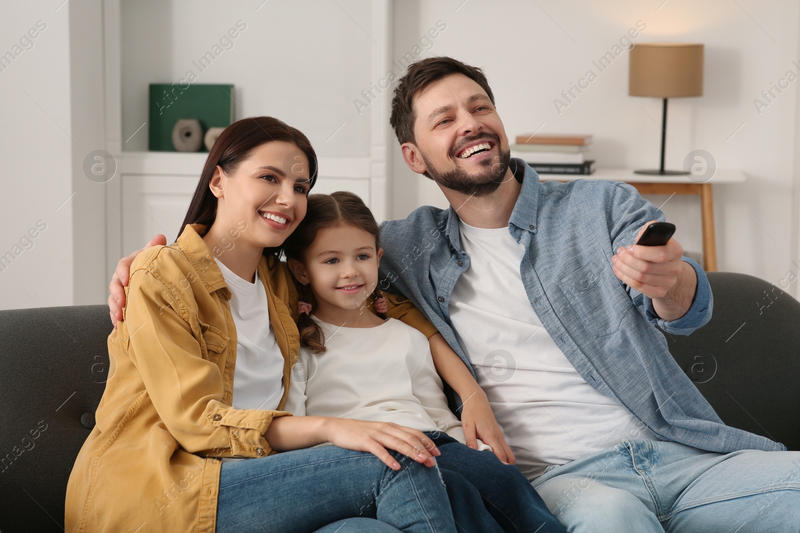 Photo of Happy family watching movie at home. Father changing TV channels with remote control