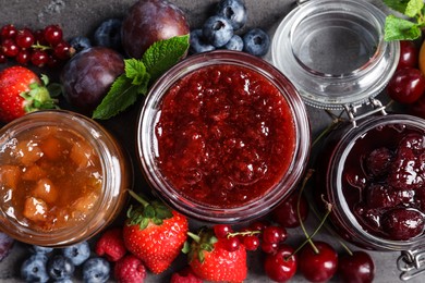 Jars with different jams and fresh fruits on grey table, flat lay