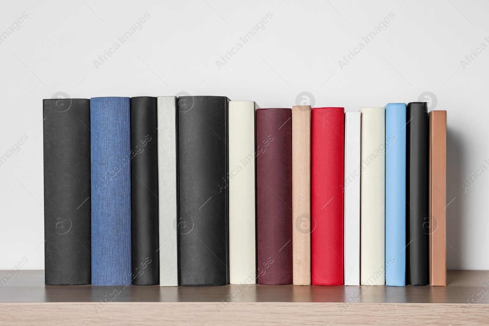 Photo of Many hardcover books on wooden table near white wall