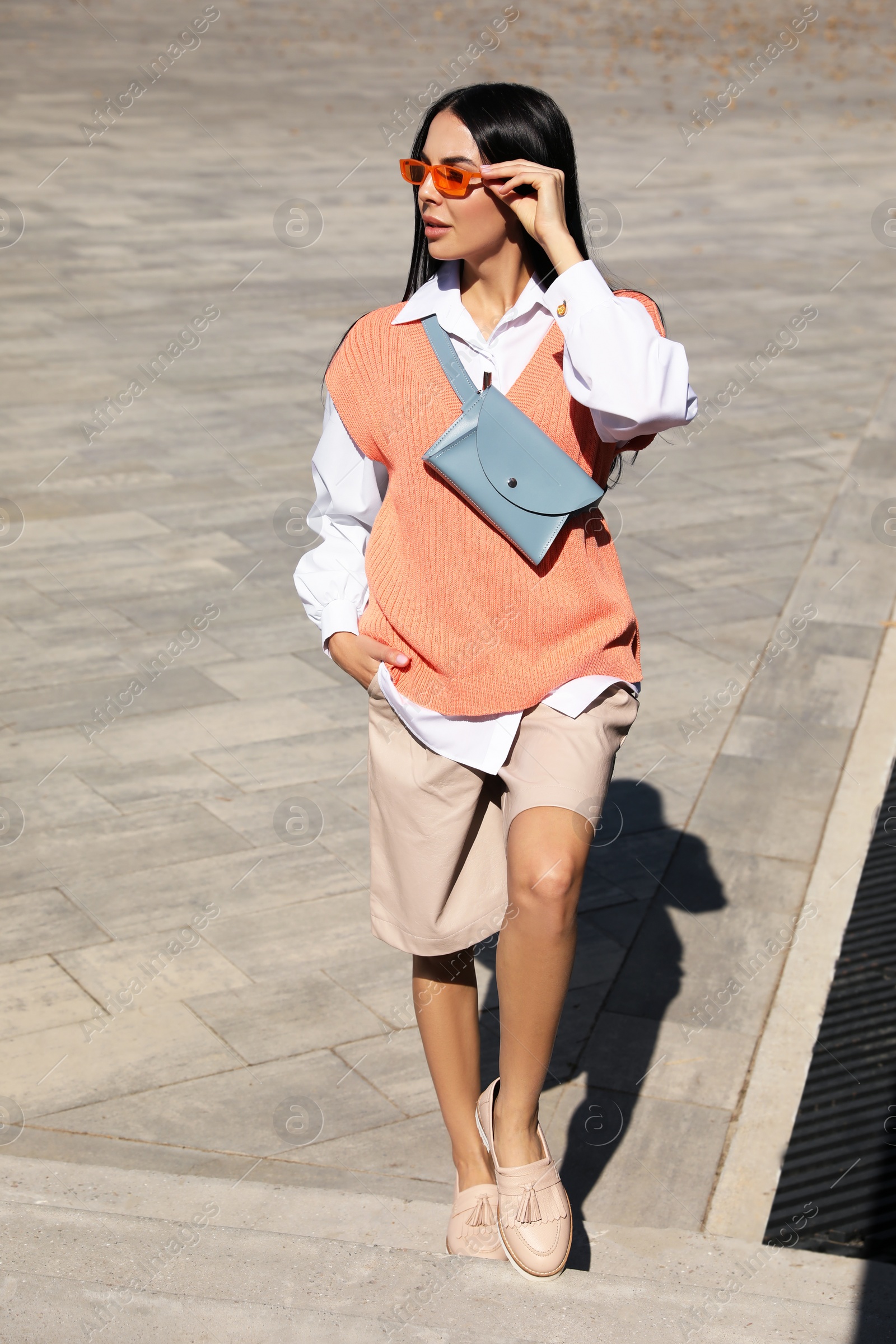 Photo of Beautiful young woman with stylish waist bag on stairs outdoors