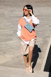 Beautiful young woman with stylish waist bag on stairs outdoors