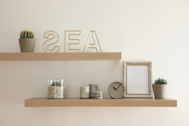 Photo of Wooden shelves with plants and decorative elements on light wall