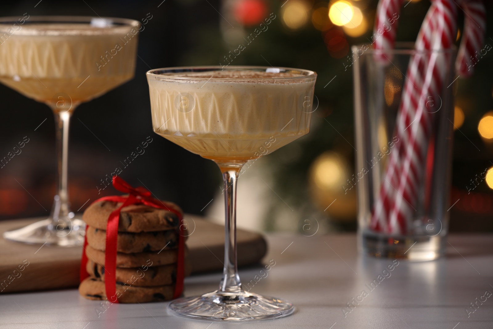 Photo of Tasty eggnog, cookies and candy canes on white marble table against blurred festive lights, closeup