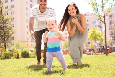 Photo of Parents supporting their baby daughter while she learning to walk outdoors