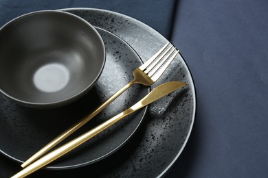 Photo of Stylish ceramic plates, bowl and cutlery on dark blue background, closeup