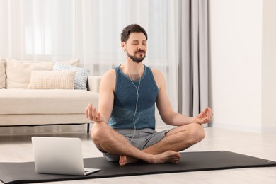 Man in sportswear meditating near laptop at home. Harmony and zen