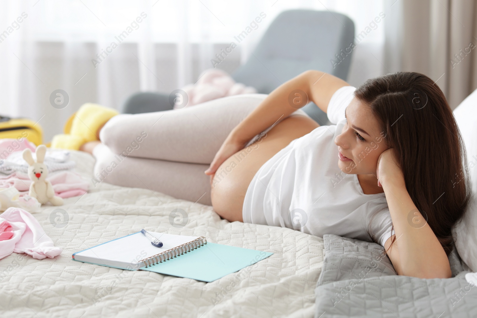 Photo of Pregnant woman writing packing list for maternity hospital on bed at home