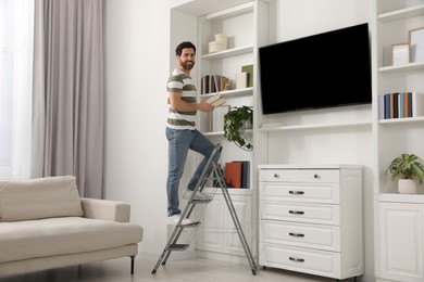 Photo of Happy man with books on metal folding ladder at home