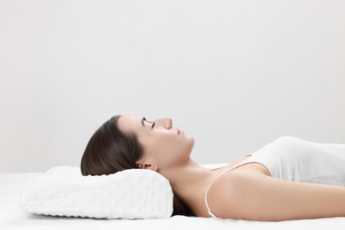 Photo of Woman sleeping on orthopedic pillow against light grey background, space for text