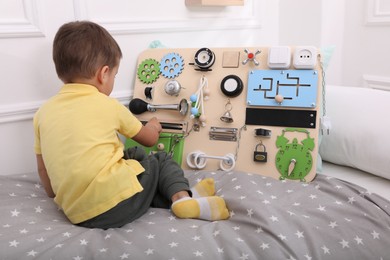 Little boy playing with busy board on bed at home