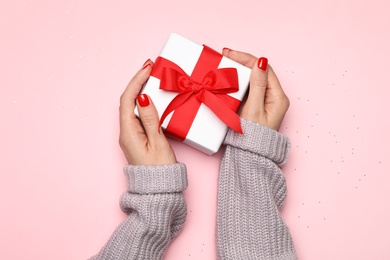 Young woman holding Christmas gift on pink background, top view