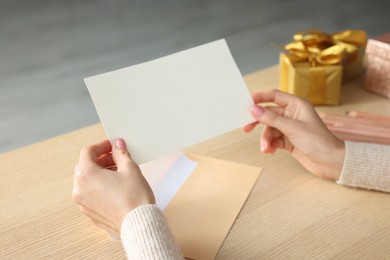 Woman holding greeting card at wooden table, closeup