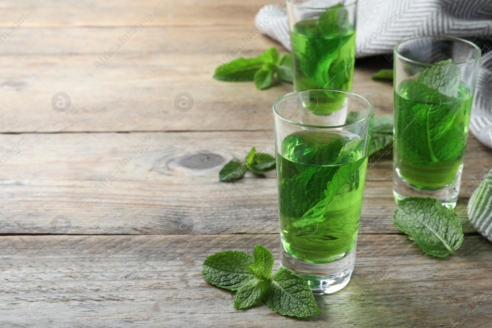 Photo of Delicious mint liqueur with green leaves on wooden table. Space for text