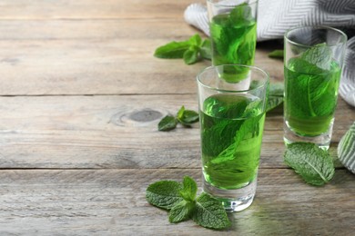 Delicious mint liqueur with green leaves on wooden table. Space for text