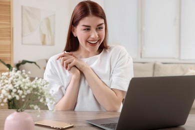 Happy woman with laptop at table in room