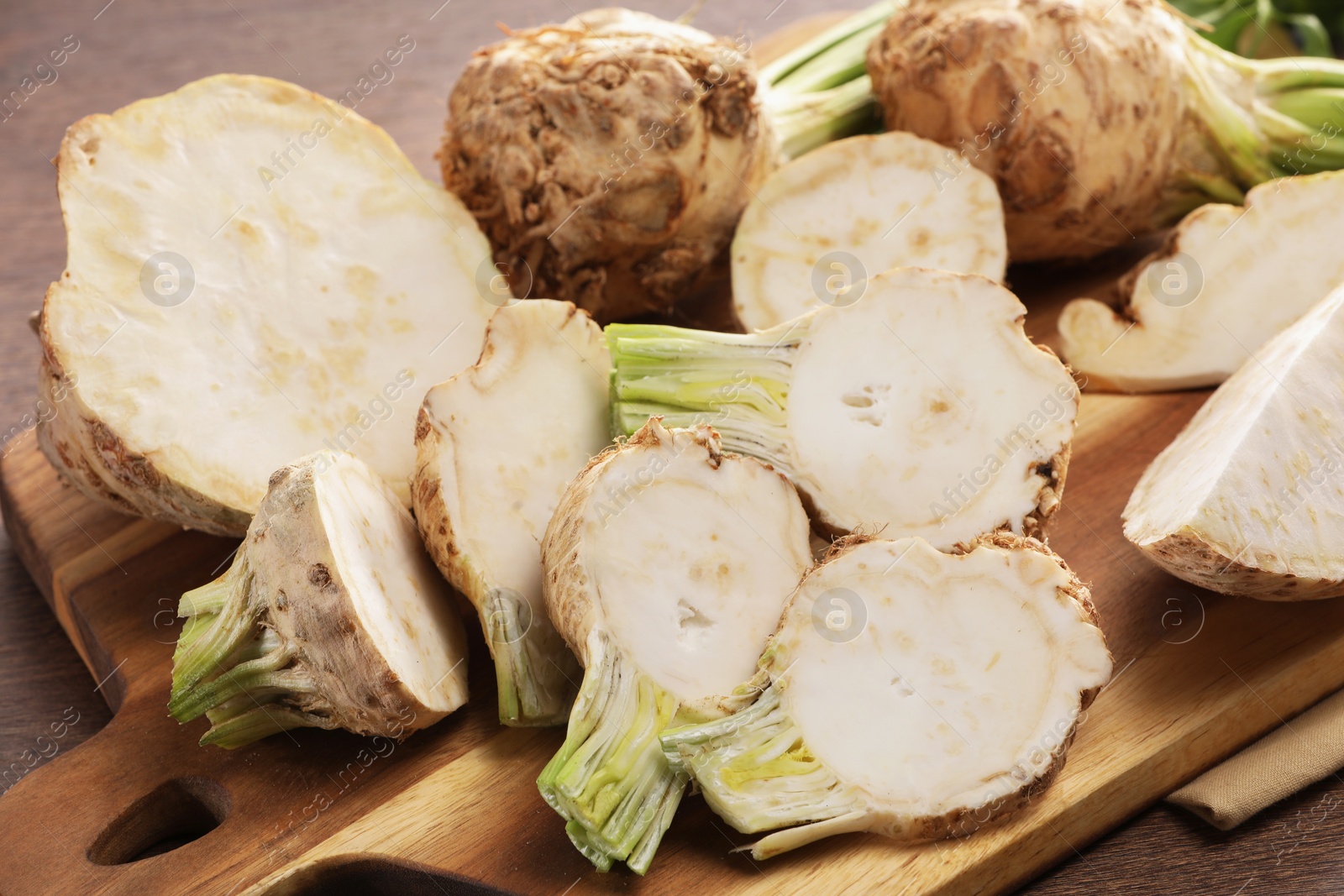 Photo of Whole and cut celery roots on wooden table, closeup