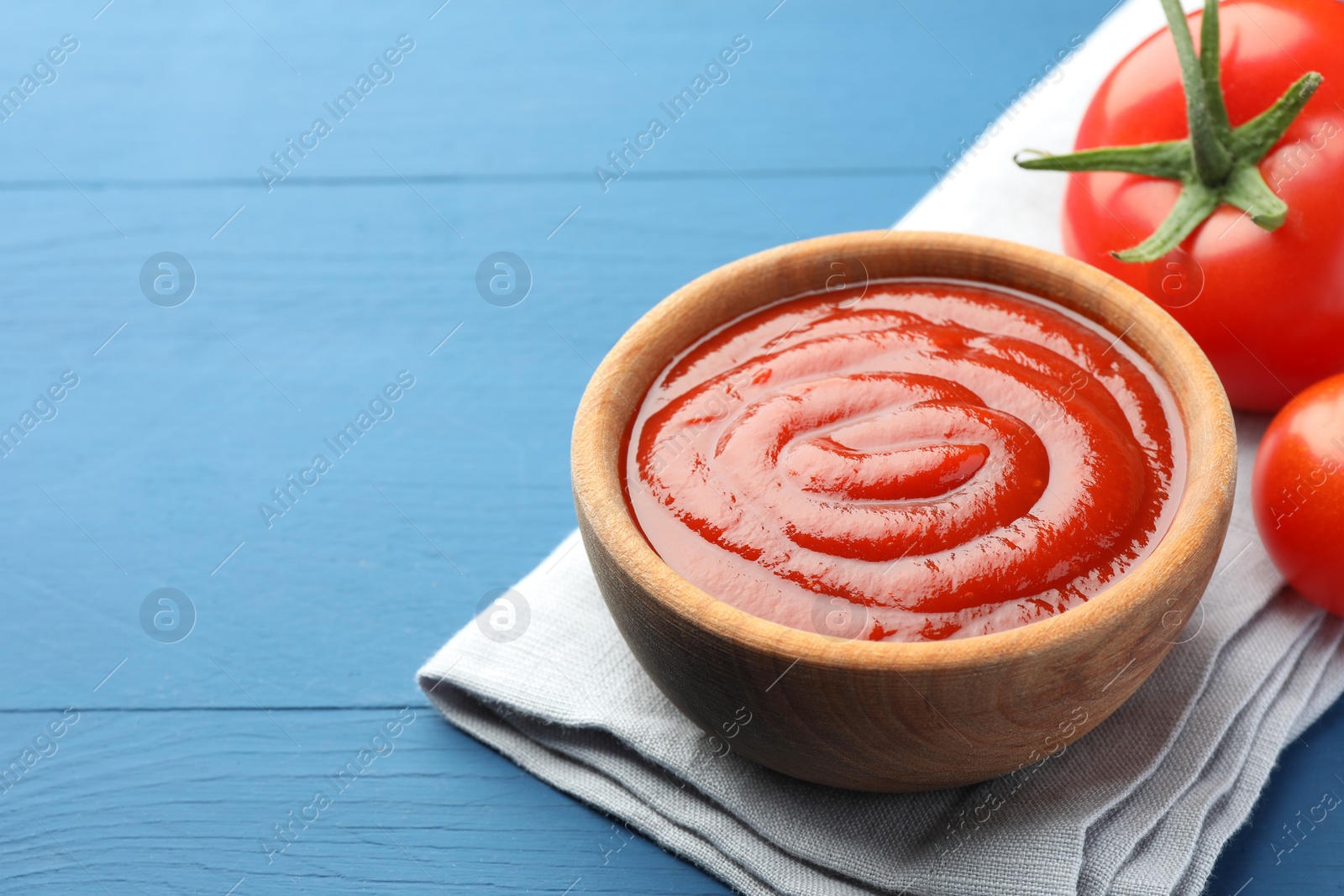 Photo of Bowl of tasty ketchup and tomatoes on blue wooden table, closeup. Space for text