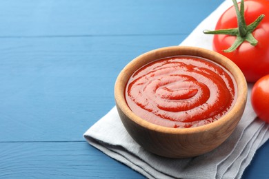 Bowl of tasty ketchup and tomatoes on blue wooden table, closeup. Space for text