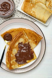 Tasty crepes with chocolate paste served on white wooden table, flat lay