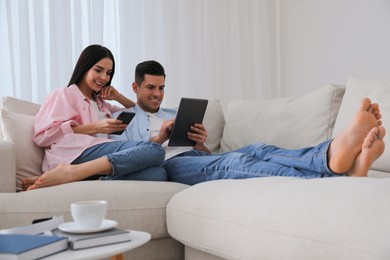 Photo of Couple with gadgets resting on sofa in living room