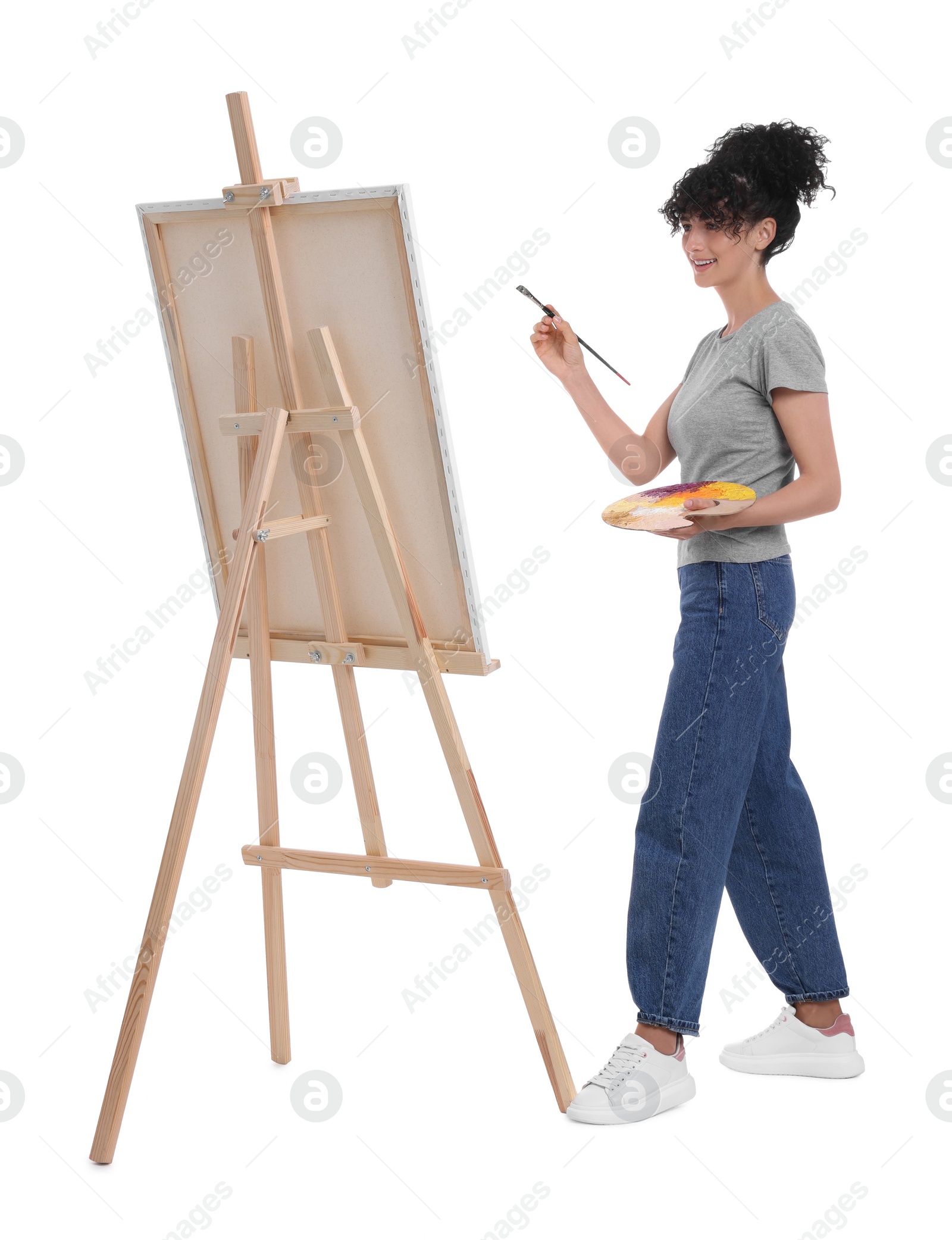 Photo of Young woman painting on easel with canvas against white background