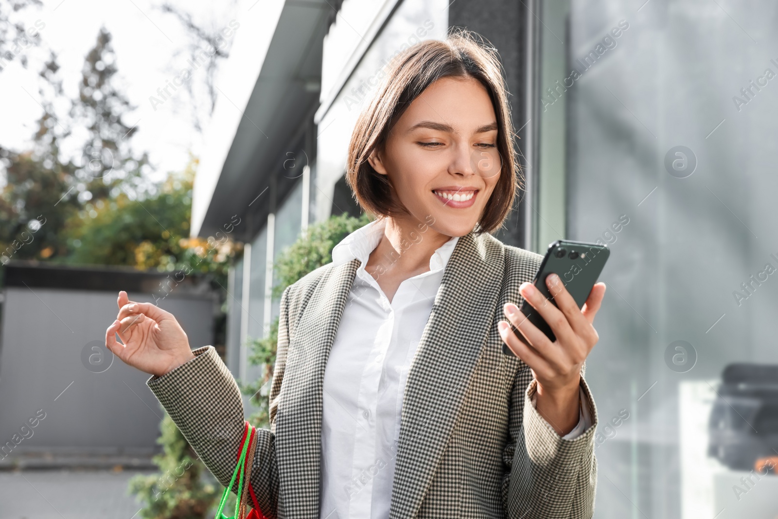 Photo of Special Promotion. Happy young woman with shopping bags and smartphone on city street
