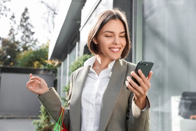 Photo of Special Promotion. Happy young woman with shopping bags and smartphone on city street