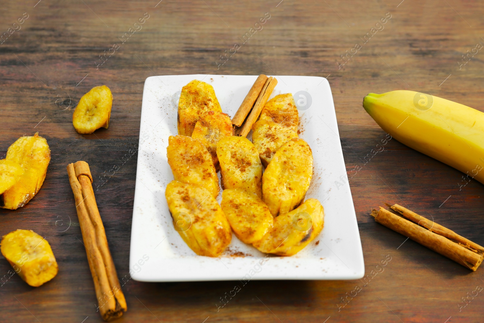 Photo of Tasty deep fried banana slices and cinnamon sticks on wooden table