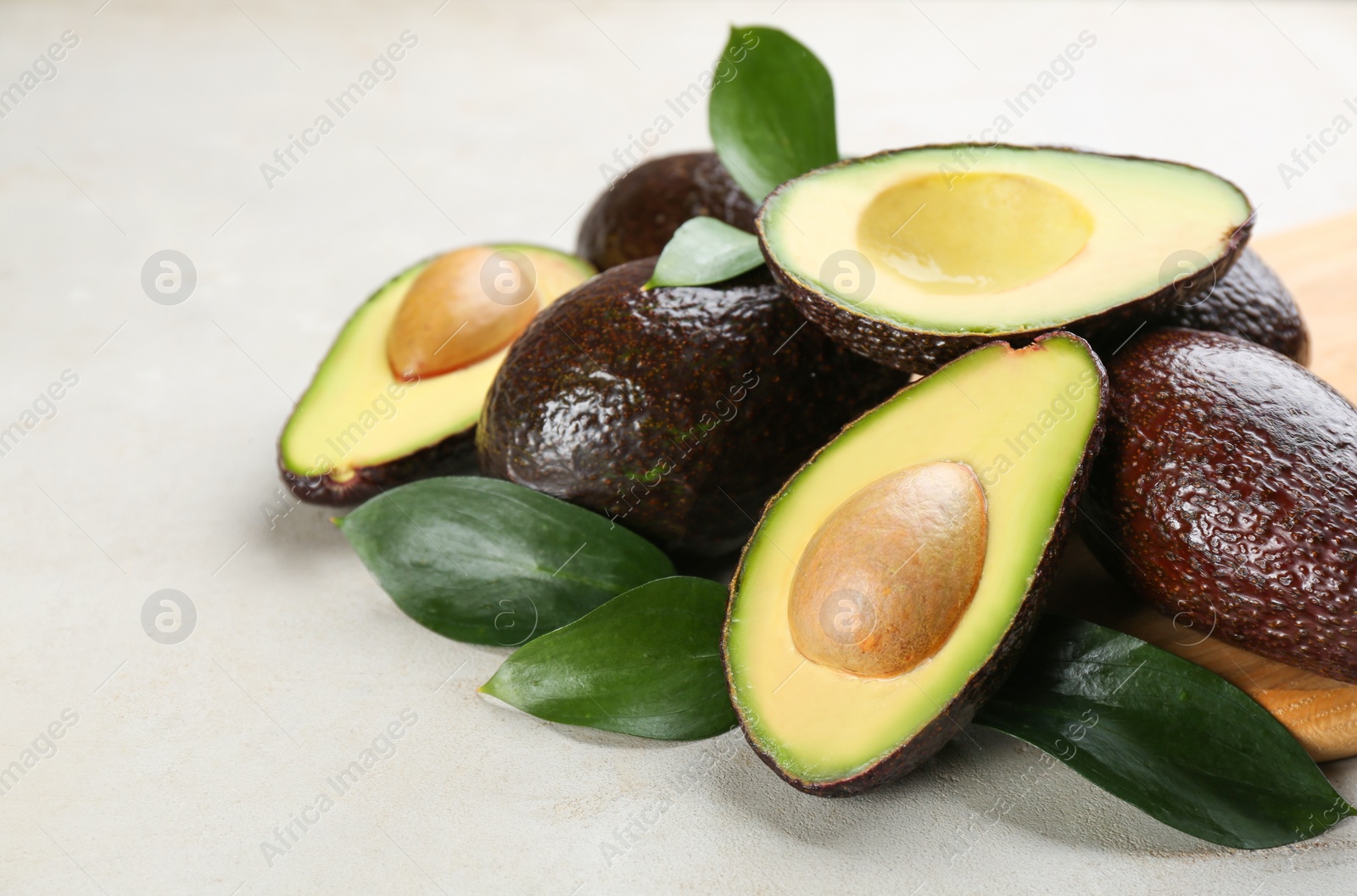 Photo of Whole and cut avocados with green leaves on light table, closeup