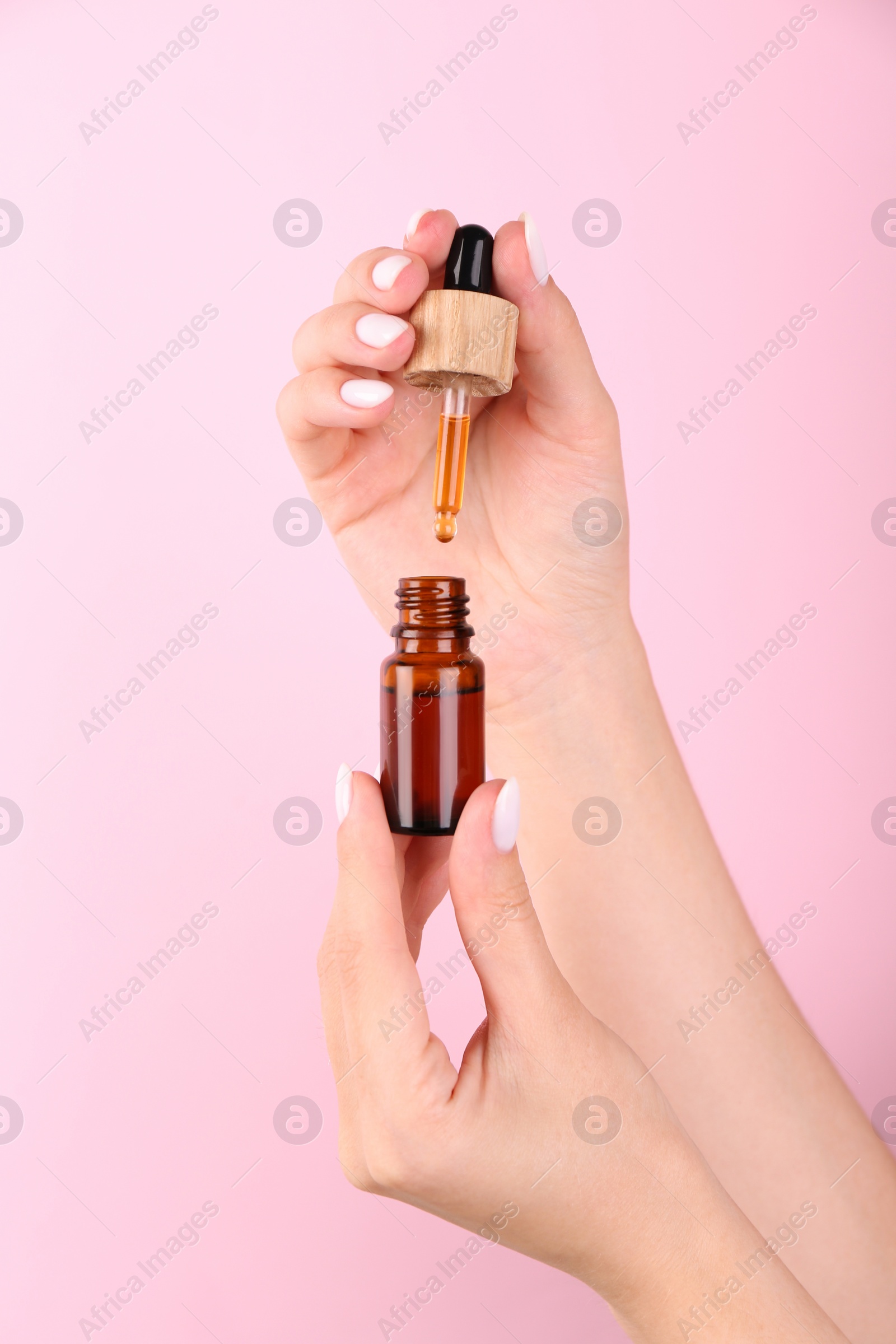 Photo of Woman holding bottle of essential oil on pink background, closeup