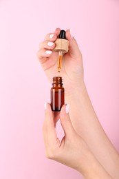 Woman holding bottle of essential oil on pink background, closeup