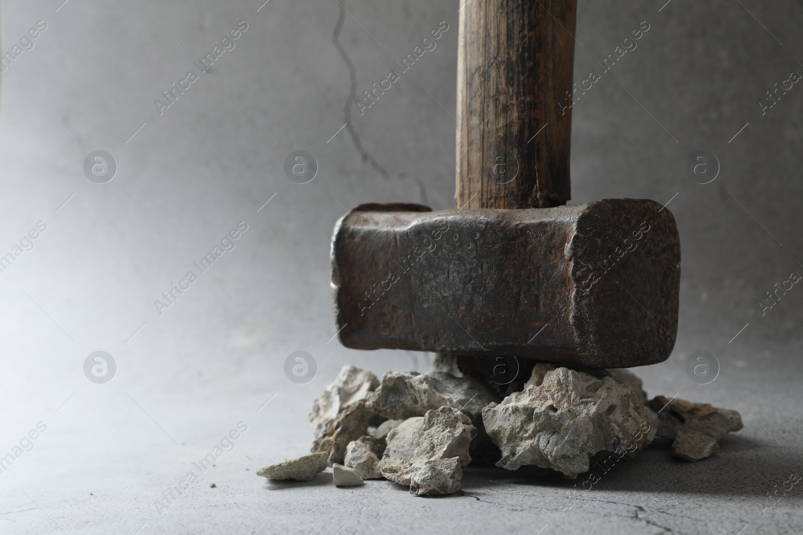 Photo of One sledgehammer and pieces of broken stones on grey background, closeup. Space for text