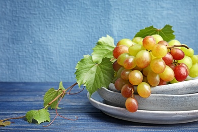 Photo of Fresh ripe juicy grapes in dishware on table against color background with space for text