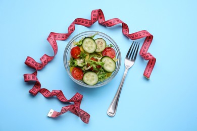 Measuring tape, salad and fork on light blue background, flat lay