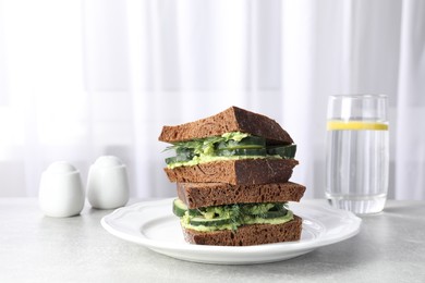 Photo of Tasty sandwiches with cucumber, cream cheese, dill and glass of lemon water on grey table indoors, space for text
