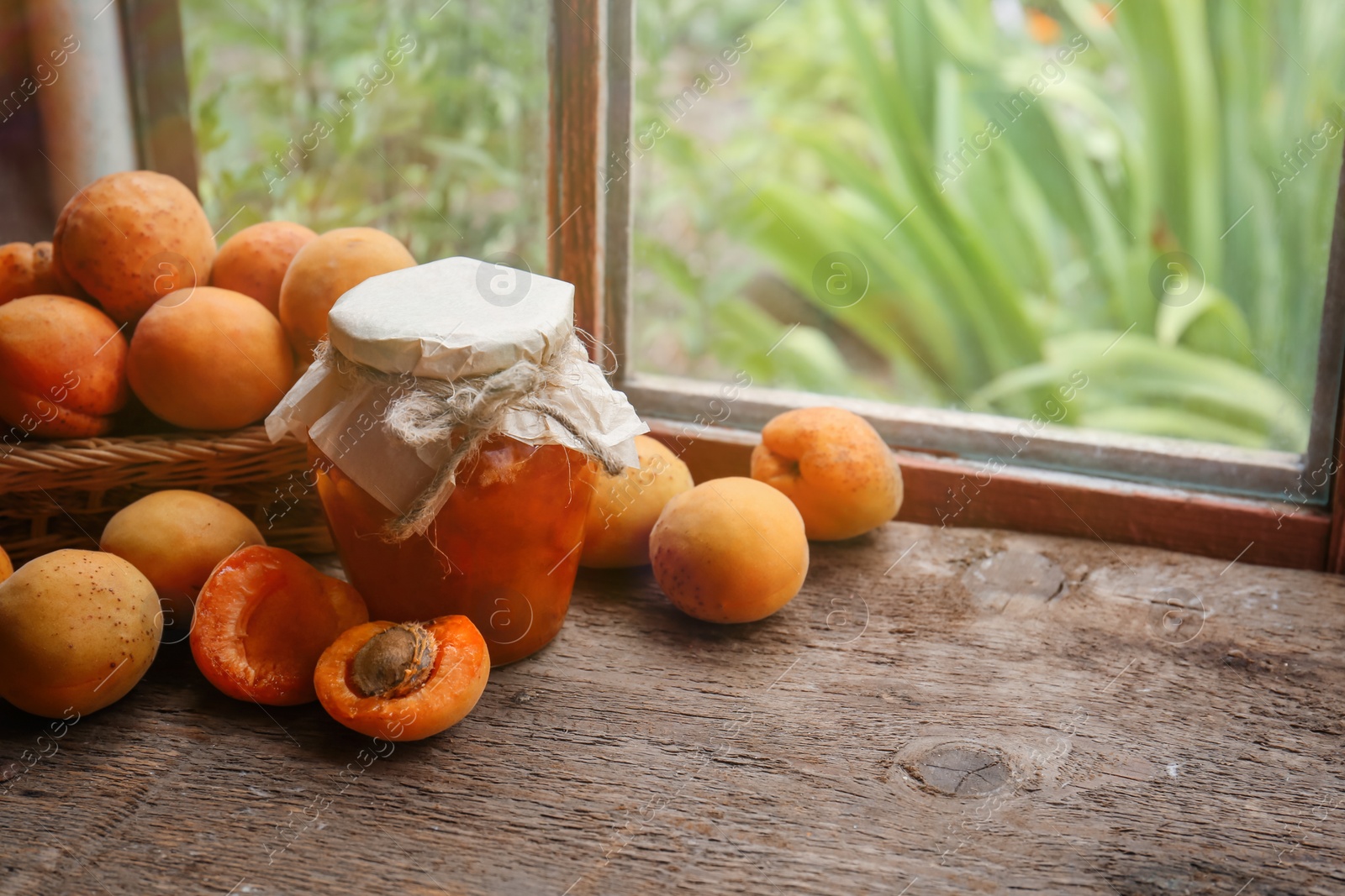 Photo of Jar of delicious jam and fresh ripe apricots on wooden table indoors. Fruit preserve