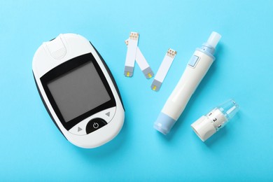 Photo of Digital glucometer, lancet pen and test strips on light blue background, flat lay. Diabetes control