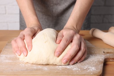 Woman kneading dough at wooden table near white brick wall, closeup