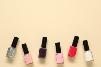 Bright nail polishes in bottles on beige background, flat lay. Space for text